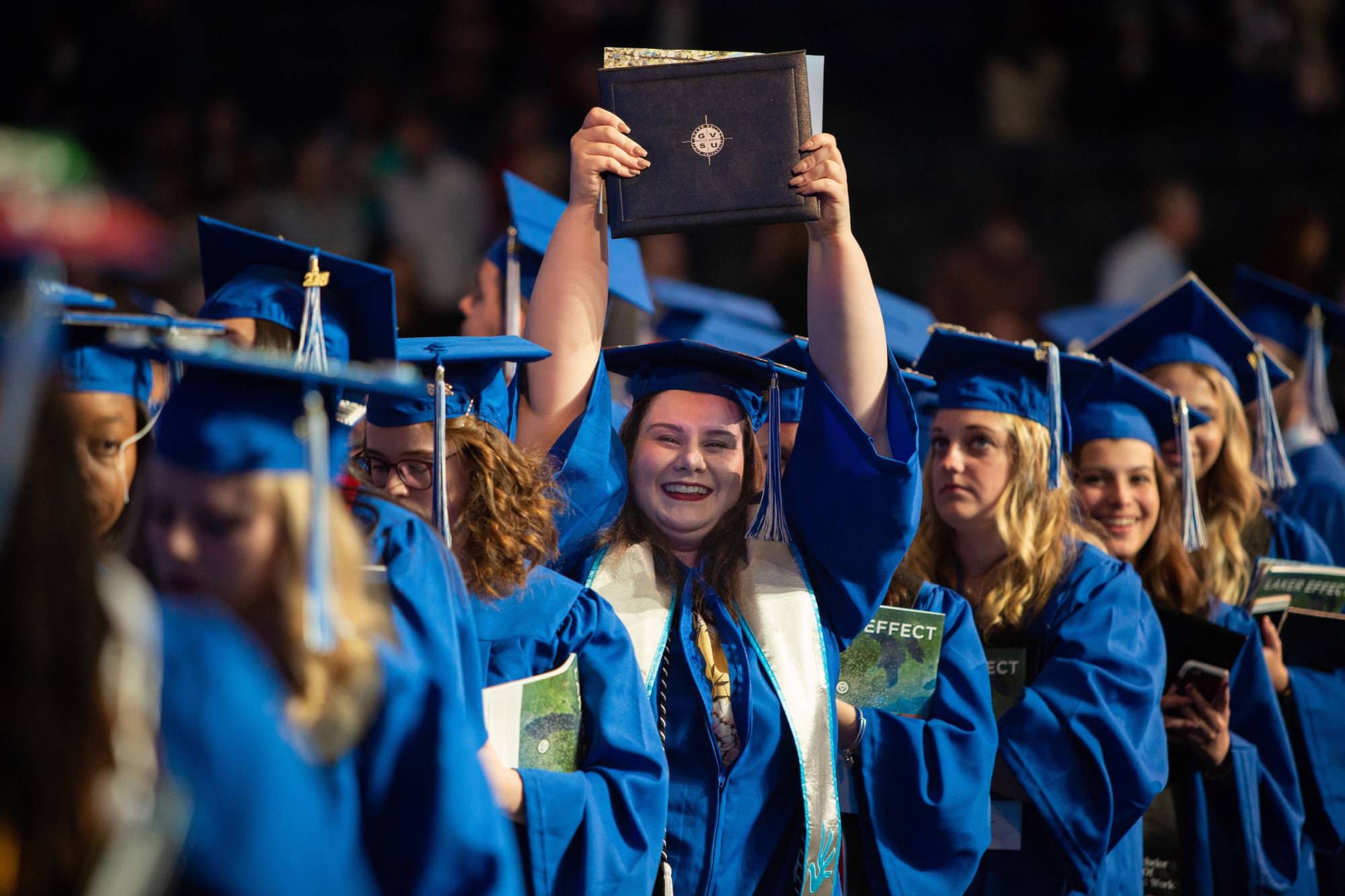 Student proudly holding diploma above her head after graduating from Grand Valley